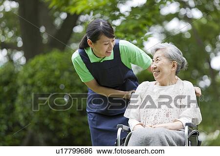 Stock Photograph - Healthcare worker pushing senior woman in wheelchair, Tokyo Prefecture, Honshu, Japan. Fotosearch