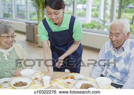 Stock Photograph - Healthcare worker serving food to senior woman, Kanagawa Prefecture, Honshu, Japan. Fotosearch