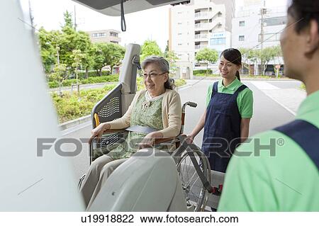 Stock Image - Healthcare workers helping senior woman in wheelchair getting into a van, Kanagawa Prefecture, Honshu, Japan. Fotosearch