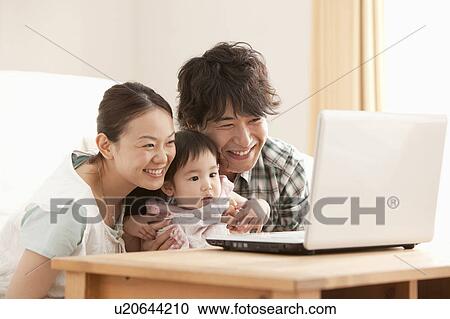 Stock Image - Mother, Father and Baby Girl Using Laptop. Fotosearch