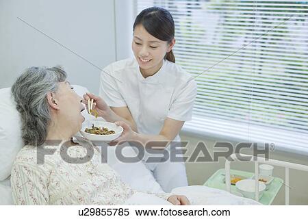 Stock Photography - Nurse helping up a senior woman eat in bed, Kanagawa Prefecture, Honshu, Japan. Fotosearch