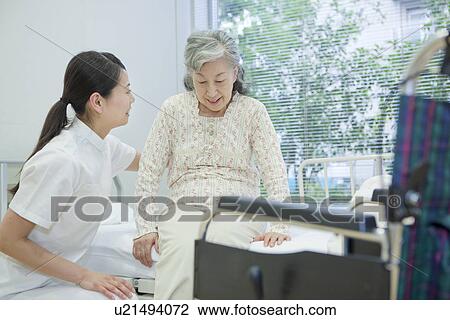 Stock Image - Nurse helping up a senior woman in bed, Kanagawa Prefecture, Honshu, Japan. Fotosearch