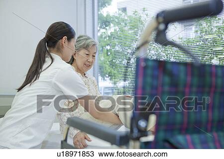 Stock Image - Nurse lifting senior woman to wheelchair from bed, Kanagawa Prefecture, Honshu, Japan. Fotosearch