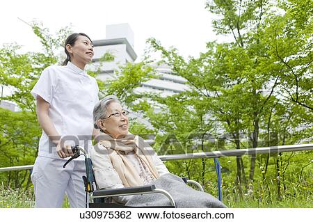 Stock Image - Nurse Pushing Senior Woman in Wheelchair. Fotosearch