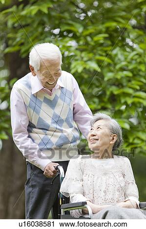 Stock Image - Senior Man Pushing Wife in Wheelchair. Fotosearch