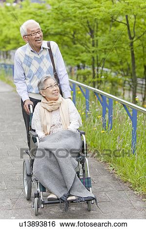 Stock Photograph - Senior Man Pushing Wife in Wheelchair. Fotosearch