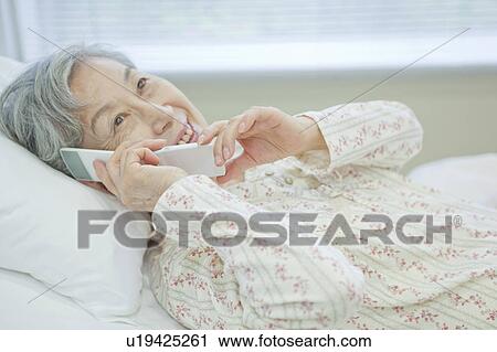 Senior woman lying on bed talking on cell phone, Kanagawa Prefecture, Honshu, Japan View Large Photo Image Stock Image - Senior woman lying on bed talking on cell phone, Kanagawa Prefecture, Honshu, Japan. Fotosearch