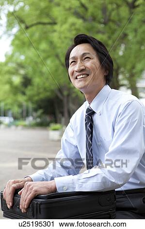 Stock Image - Businessman sitting on park bench. Fotosearch