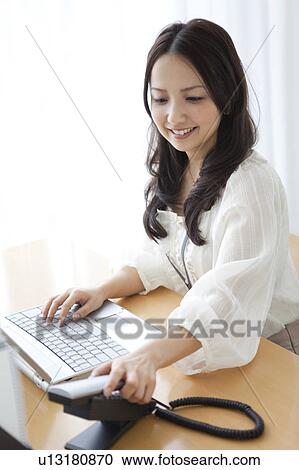 Stock Image - Businesswoman answering a landline phone. Fotosearch
