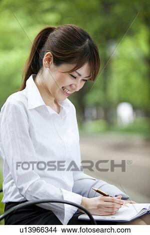 Businesswoman sitting on park bench writing on diary View Large Photo Image Picture - Businesswoman sitting on park bench writing on diary. Fotosearch