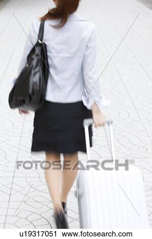 Stock Image - Businesswoman walking with suitcase. Fotosearch