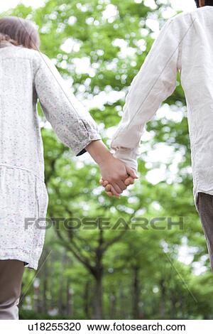 Stock Image - Couple holding hands, rear view. Fotosearch