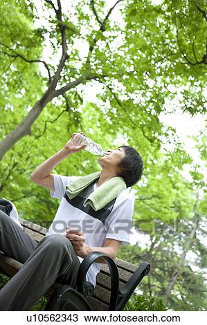 Stock Image - Man sitting on bench drinking water. Fotosearch