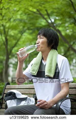 Stock Photography - Man sitting on bench drinking water. Fotosearch