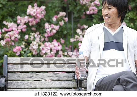 Man sitting on bench holding bottled water View Large Photo Image Stock Image - Man sitting on bench holding bottled water. Fotosearch