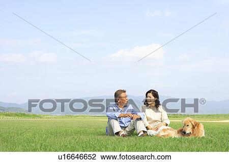 Stock Image - Mature Couple with Dog Sitting in Field. Fotosearch