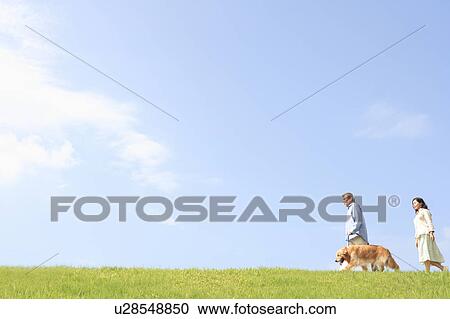 Stock Image - Mature Couple with Dog Walking in Field. Fotosearch