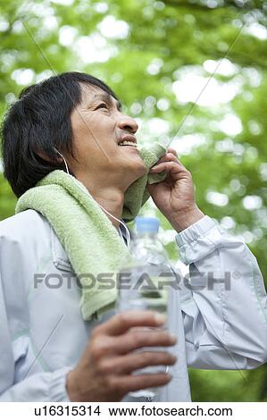 Mature man listening to music and holding water bottle View Large Photo Image Picture - Mature man listening to music and holding water bottle. Fotosearch