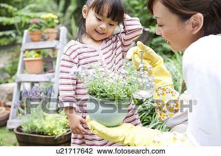 Stock Image - Mother and daughter spraying water on potted flower. Fotosearch