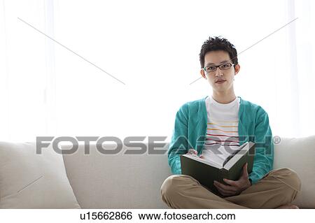 Portrait of a young man sitting on sofa View Large Photo Image Stock Photograph - Portrait of a young man sitting on sofa. Fotosearch