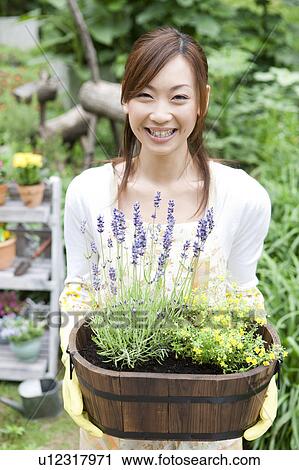 Stock Image - Portrait of young woman holding potted flowers. Fotosearch