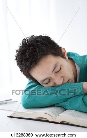 Stock Photo - Young man falling asleep while studying. Fotosearch