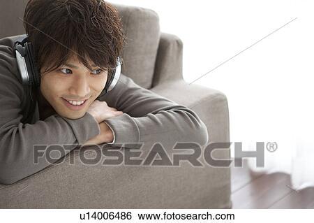 Young man lying on front listening to music View Large Photo Image Stock Photograph - Young man lying on front listening to music. Fotosearch