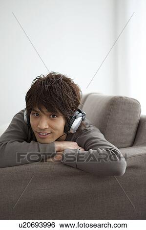 Stock Photograph - Young man lying on front listening to music. Fotosearch