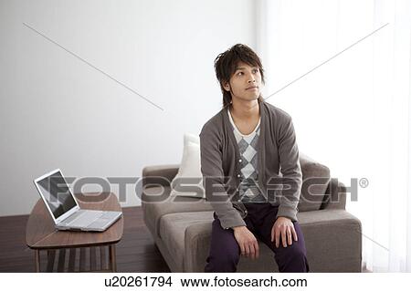 Picture - Young man sitting on sofa looking up. Fotosearch