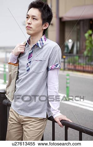 Young man standing outdoors leaning on a fence View Large Photo Image Stock Photography - Young man standing outdoors leaning on a fence. Fotosearch
