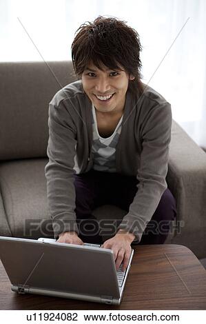 Young man using laptop on sofa View Large Photo Image Stock Image - Young man using laptop on sofa. Fotosearch