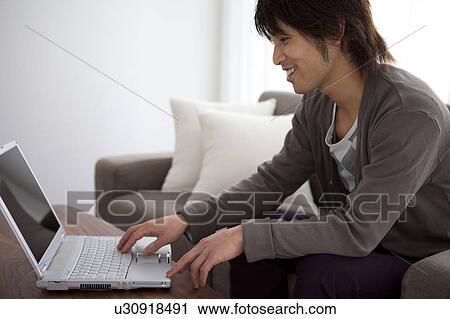 Stock Image - Young man using laptop on sofa. Fotosearch