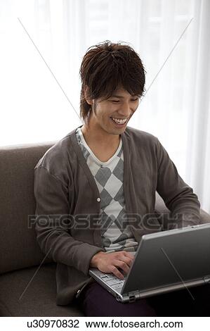Young man using laptop on sofa View Large Photo Image Stock Image - Young man using laptop on sofa. Fotosearch