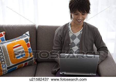 Young man using laptop on sofa View Large Photo Image Stock Photo - Young man using laptop on sofa. Fotosearch