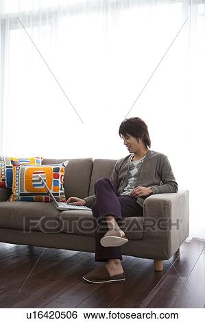 Stock Photograph - Young man using laptop on sofa. Fotosearch
