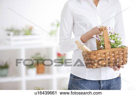 Stock Image - Young woman carrying a basket with potted flower. Fotosearch