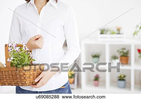 Stock Photo - Young woman carrying a basket with potted flower. Fotosearch