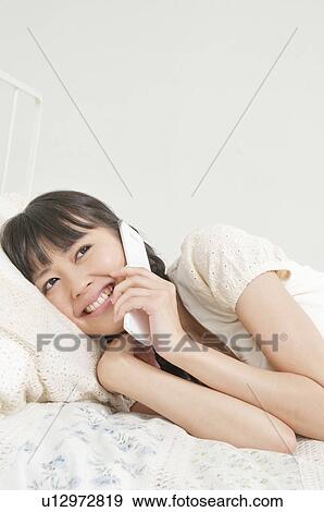 Stock Photo - Young Woman Lying on Bed and Talking on Phone. Fotosearch