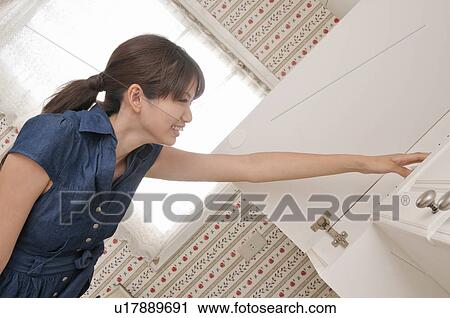 Stock Image - Young Woman Reaching for Cupboard. Fotosearch