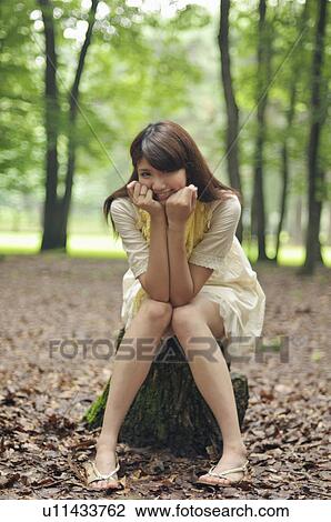 Stock Image - Young Woman Sitting on Tree Stump. Fotosearch