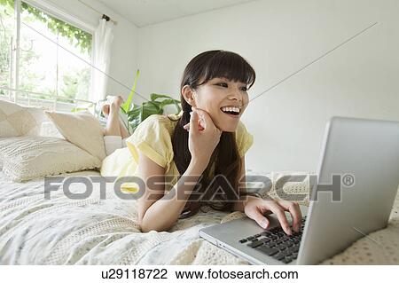 Stock Image - Young Woman Using Laptop in Bed. Fotosearch