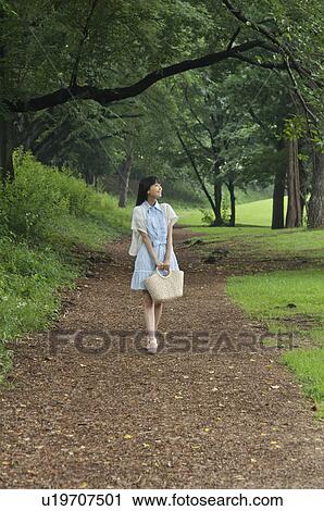 Stock Image - Young Woman Walking in Forest Path. Fotosearch