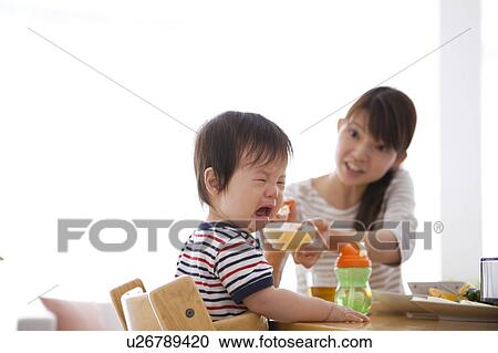 Stock Image - Baby Boy Crying Whilst Mother Offering Food. Fotosearch