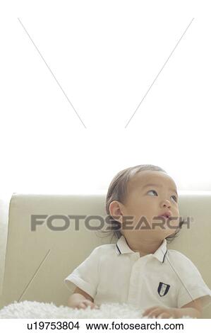 Picture - Baby girl sitting on sofa and looking away. Fotosearch