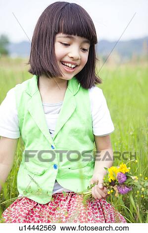 Stock Photo - Girl Sitting in Field and Holding Wildflowers. Fotosearch