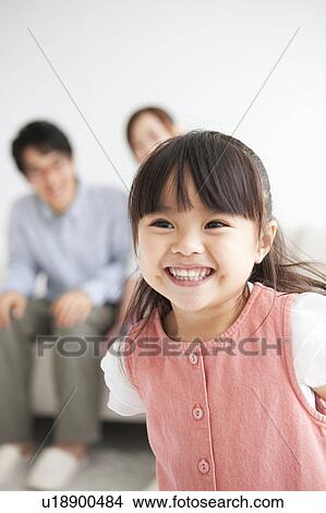 Picture - Girl smiling and parents sitting on sofa. Fotosearch