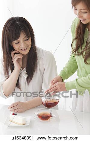 Stock Image - Mid Adult Woman Pouring Tea for Friend. Fotosearch