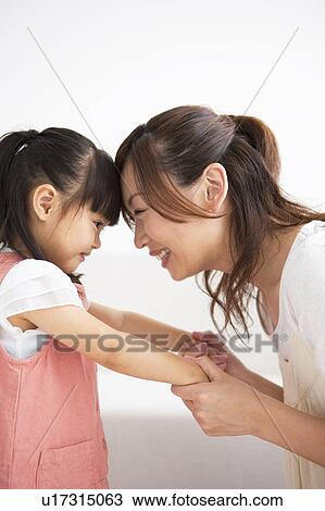 Stock Image - Mother and daughter holding hands and touching forehead. Fotosearch