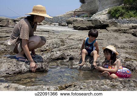 Stock Photograph - Mother and Two Children Playing on Rocky Beach. Fotosearch