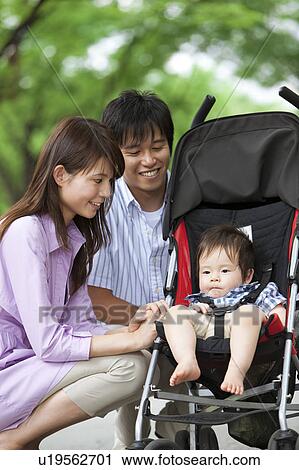 Stock Image - Parents Crouching Beside Baby Boy in Buggy. Fotosearch